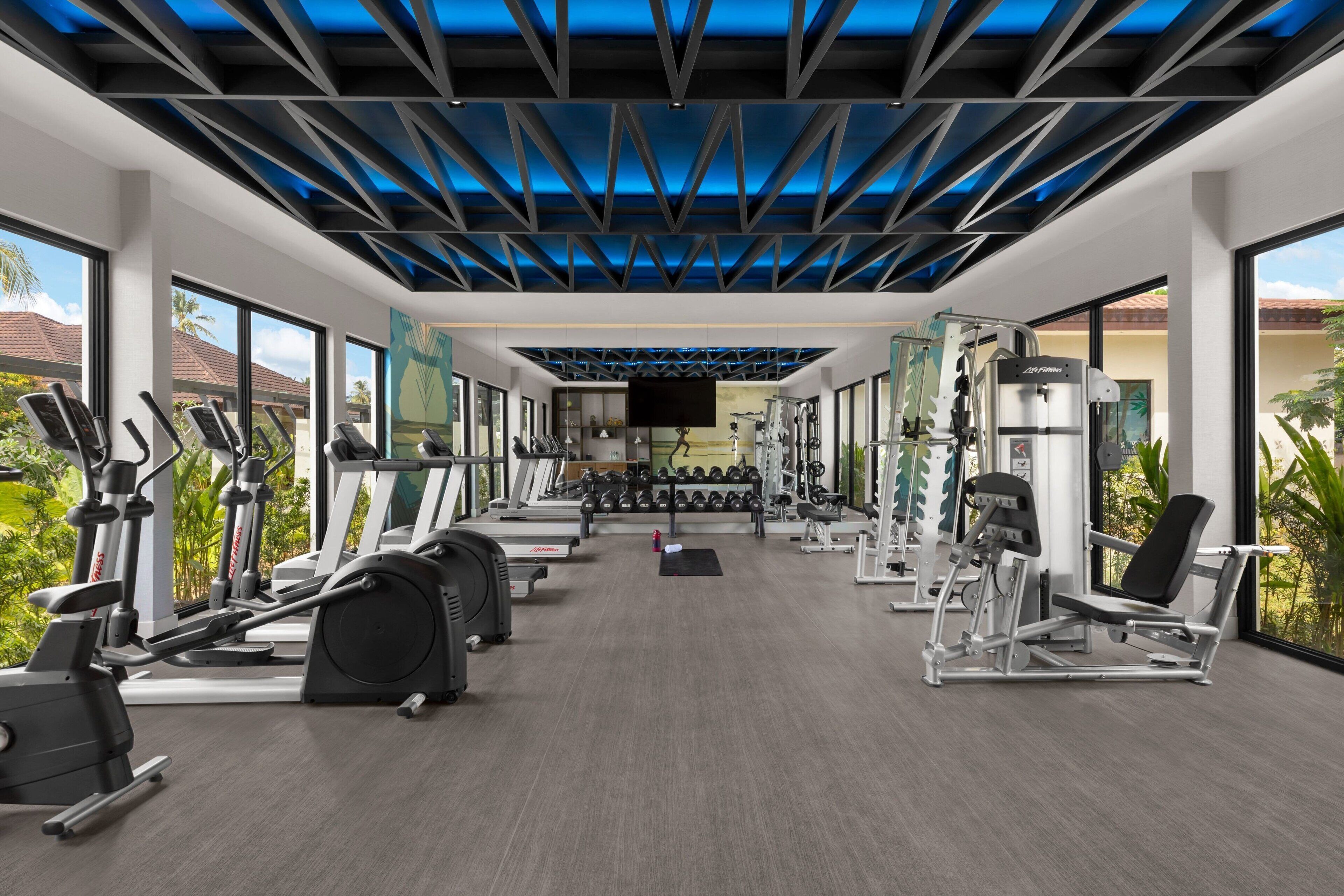 Un gimnasio moderno con máquinas de cardio, pesas libres y una pantalla de televisión.
