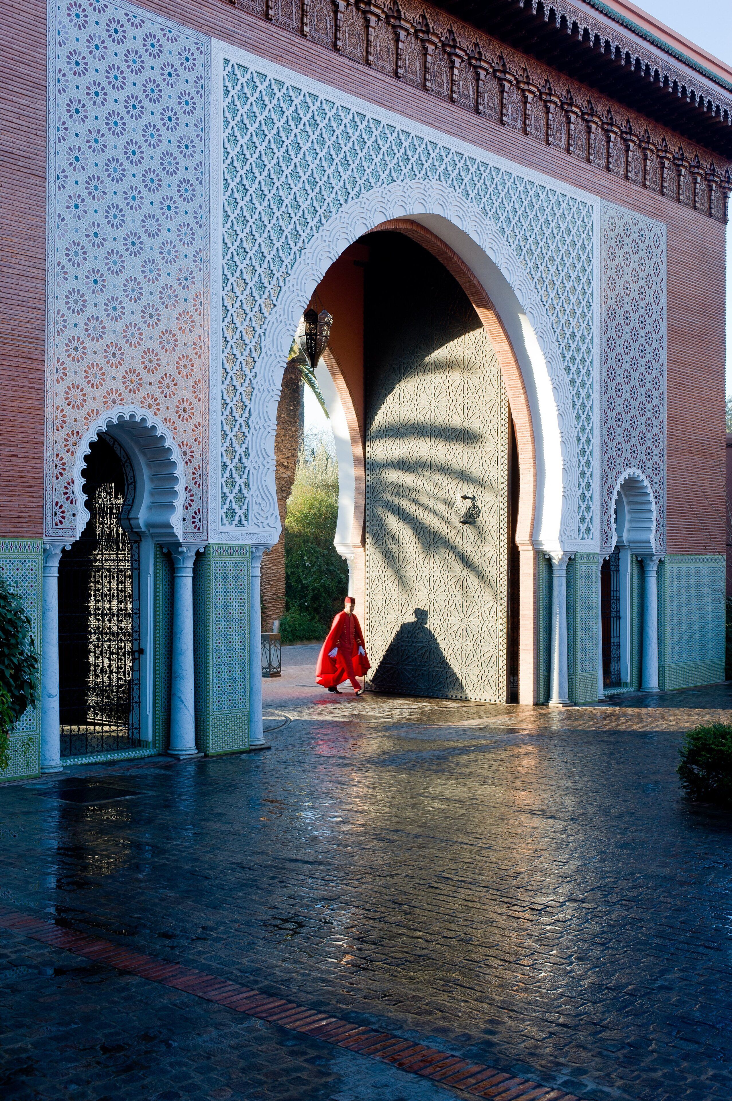 Une arche architecturale ornée de motifs complexes en mosaïque, et une personne vêtue de rouge qui la traverse.