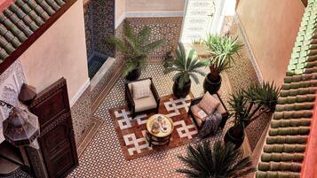A courtyard with a patterned floor, a wooden chair, a table with a tray, and potted plants.