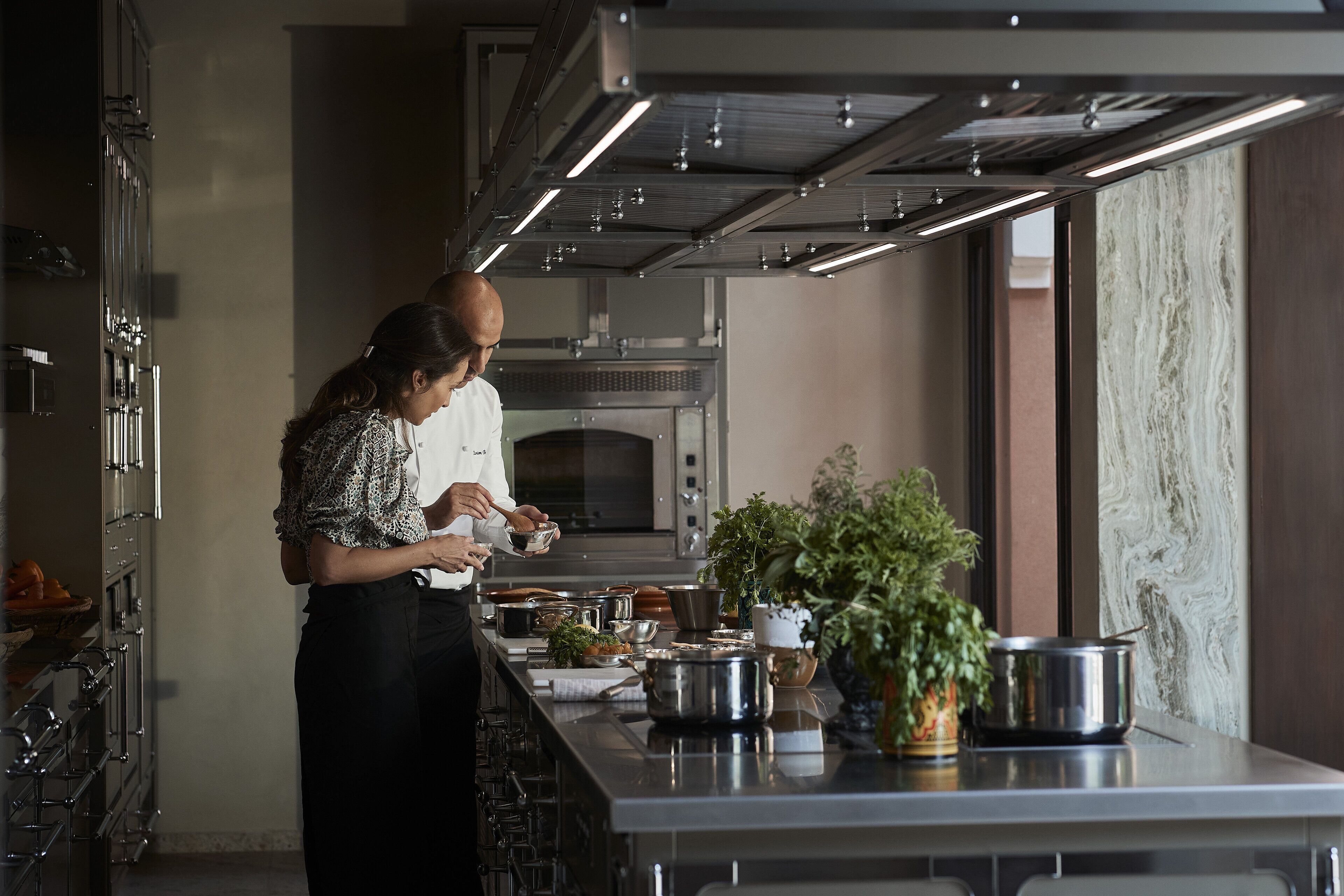 Un chef preparando comida en una cocina moderna con electrodomésticos de acero inoxidable y una encimera de mármol.
