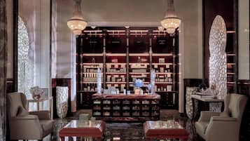 A luxurious lobby with a marble floor, two leather armchairs, a central coffee table, and a bookshelf filled with books and decorative items.