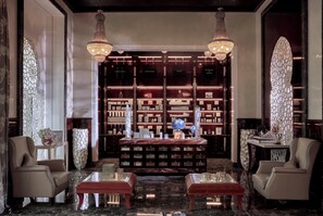 A luxurious lobby with a marble floor, two leather armchairs, a central coffee table, and a bookshelf filled with books and decorative items.