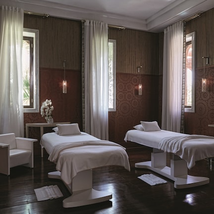 A hotel room with two beds, a sitting area, and large windows.