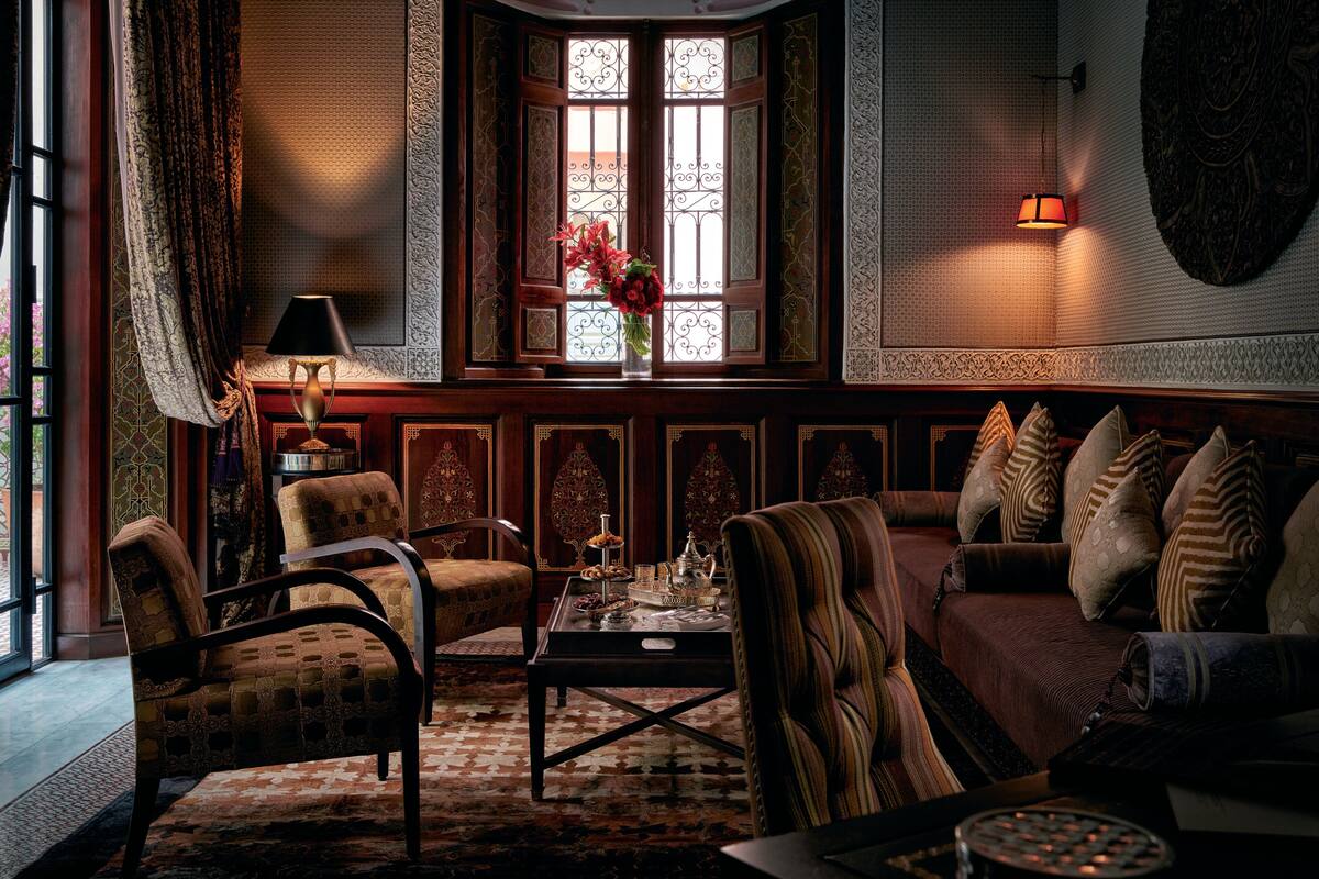Una habitación tradicional con sofá, sillones, una mesa con adornos, un jarrón con flores y una ventana de diseño intrincado.
