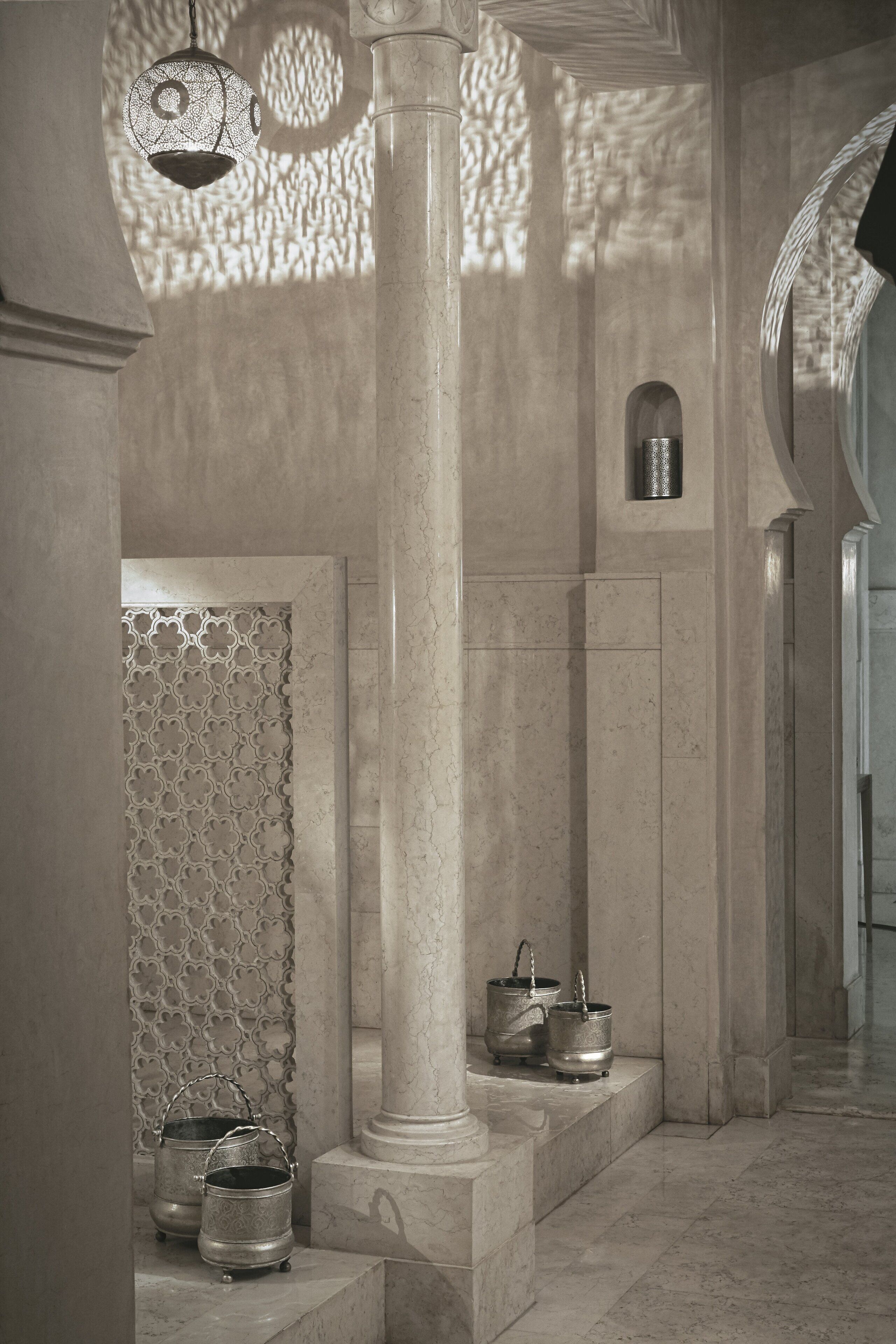 A corridor with marble columns, a patterned wall, and metal buckets on a ledge.