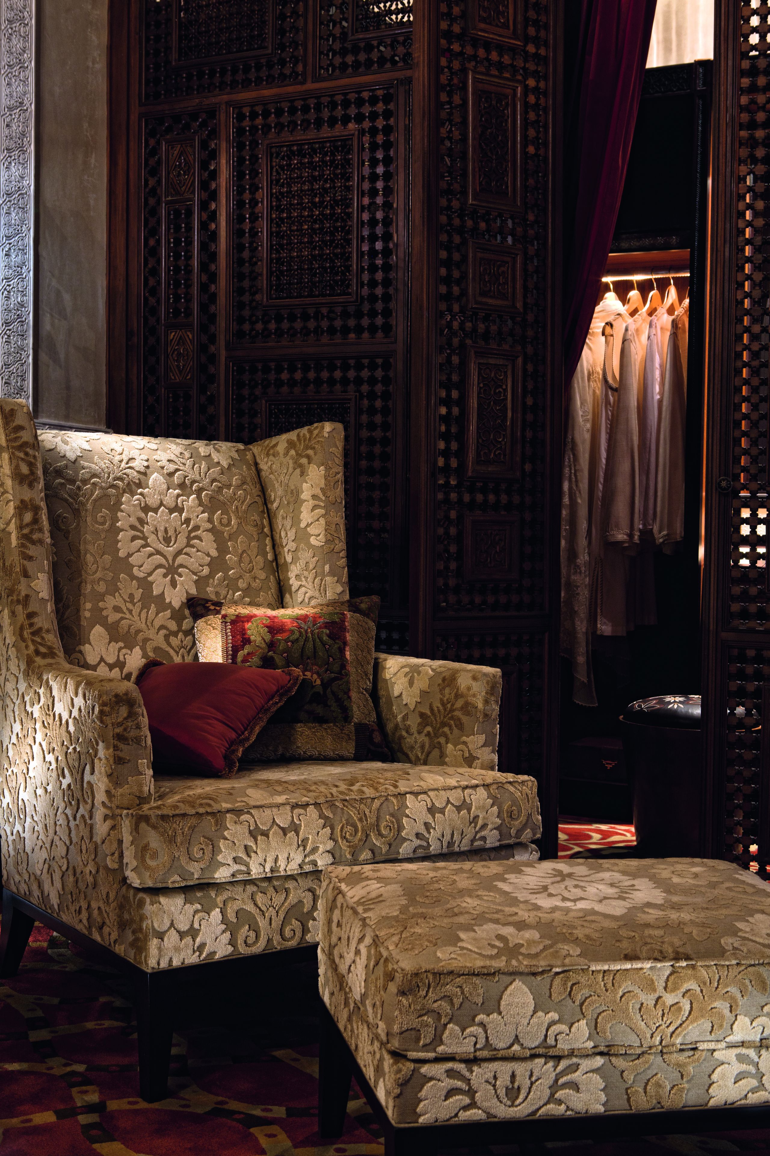 A traditional room with a patterned sofa, a matching ottoman, and a clothing rack with hanging garments.