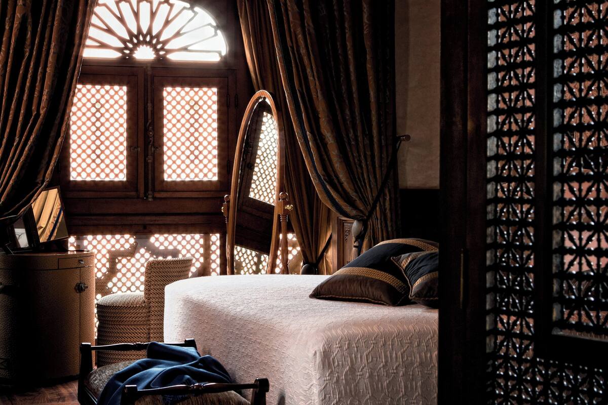 Una habitación tradicional con cama, cortinas y ventana con diseño de celosía.