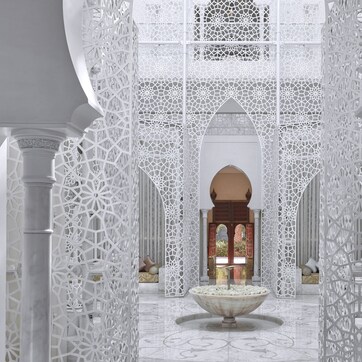 An ornate interior with intricate white lattice work, a central fountain, and a view of a traditional archway.