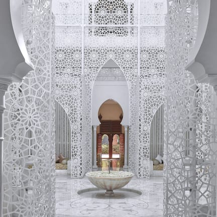 An ornate interior with intricate white lattice work, a central fountain, and a view of a traditional archway.