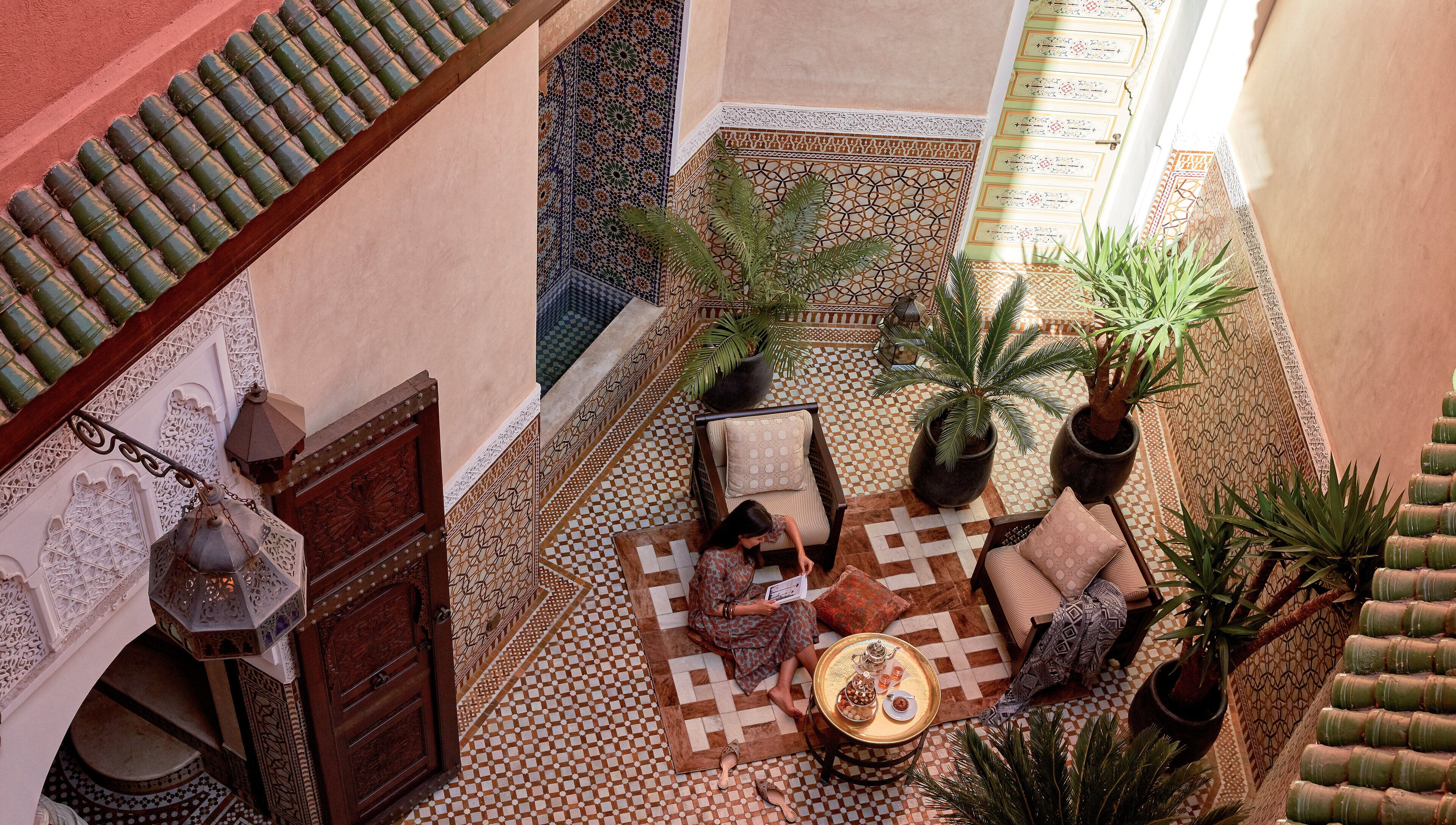 Un patio con piso de tablones, una zona de estar con cojines y plantas en macetas.