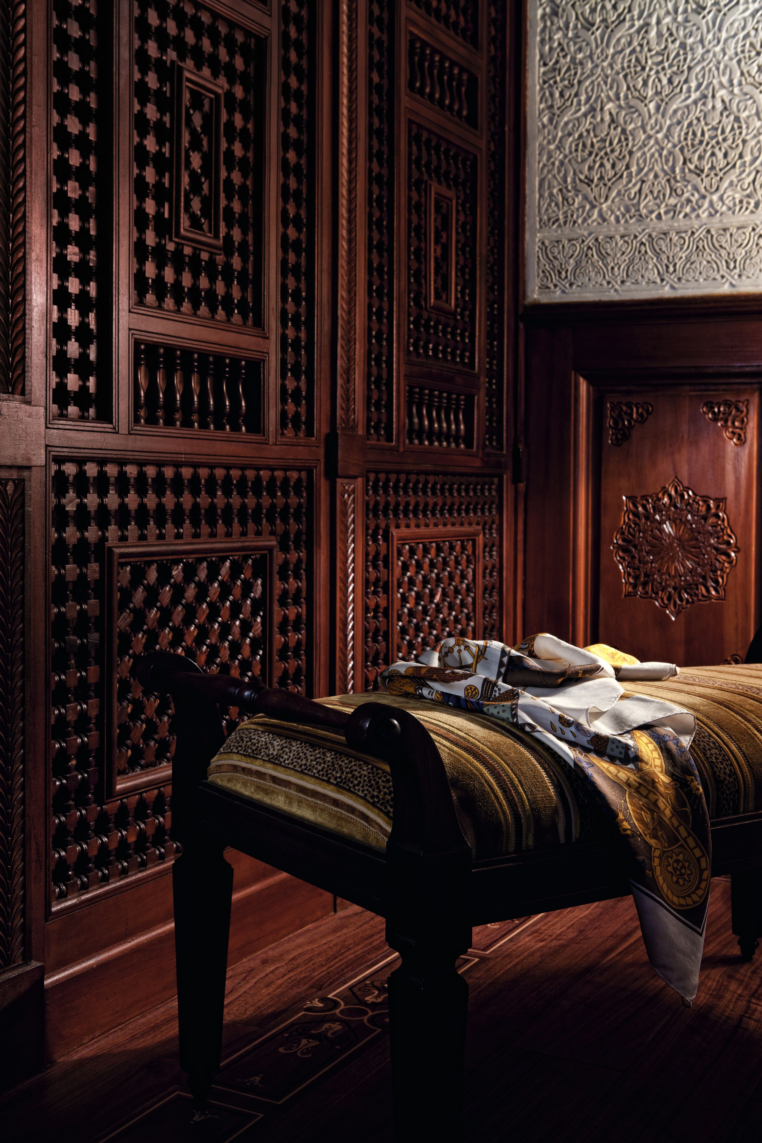 Una habitación con pared de paneles de madera, alfombra estampada y cama con cabecera decorativa.