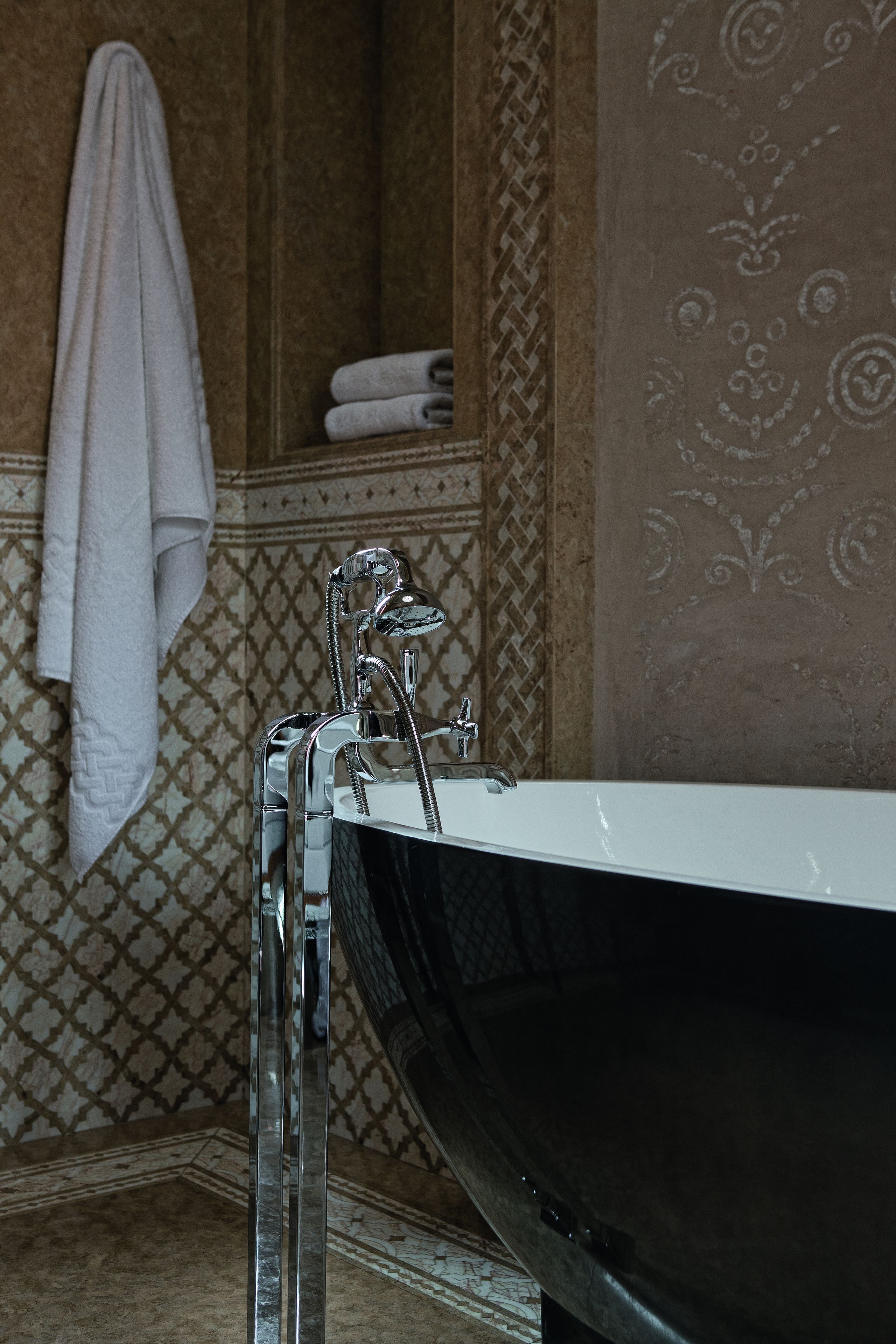 A bathroom with a freestanding bathtub, a towel rack with a folded towel, and patterned wall tiles.