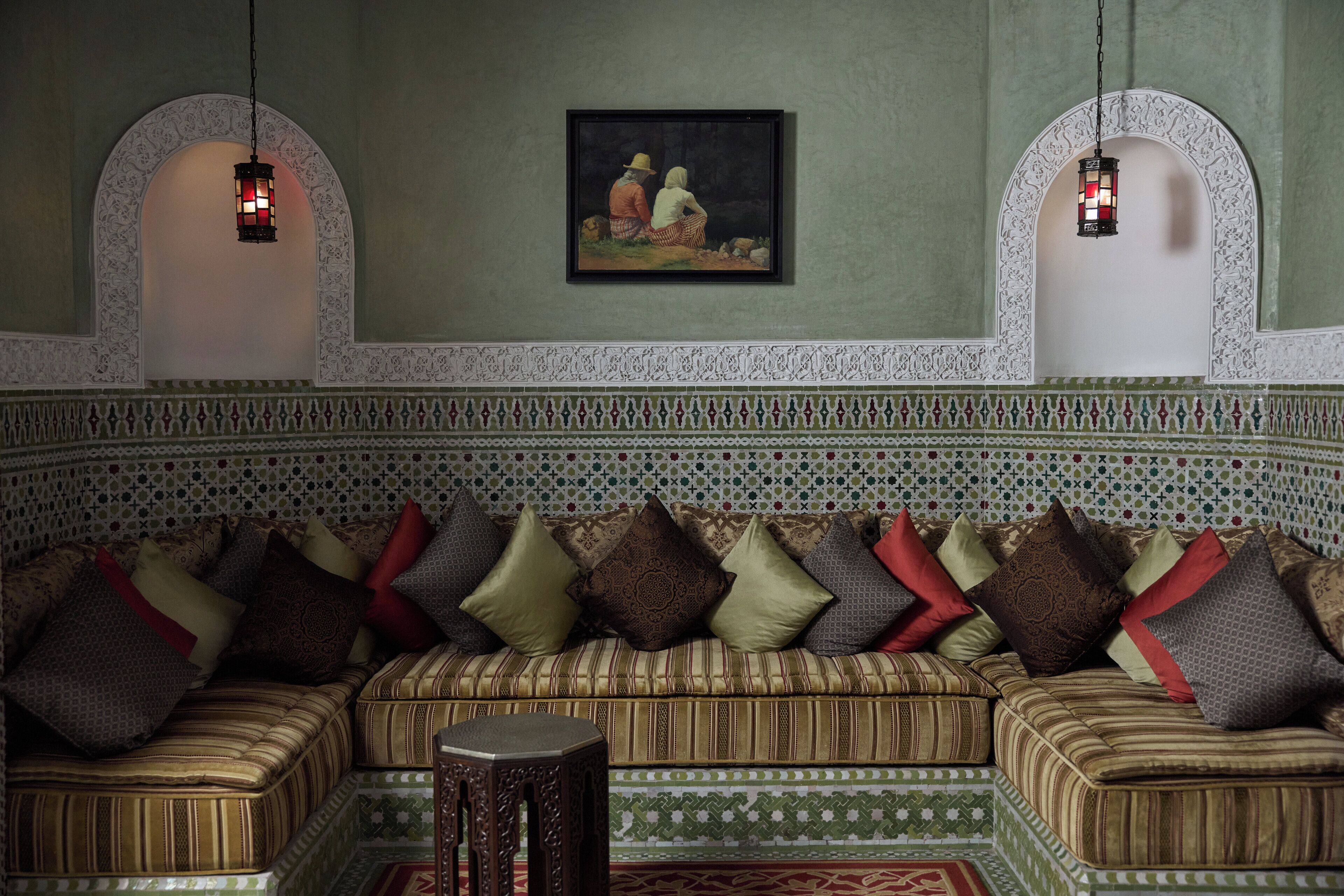 Una habitación de estilo marroquí tradicional con un sofá estampado, un taburete de madera pequeño y dos faroles colgados en la pared.