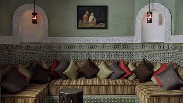 Una habitación de estilo marroquí tradicional con un sofá estampado, un taburete de madera pequeño y dos faroles colgados en la pared.