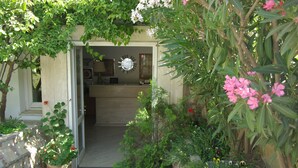 Ein Garteneingang mit einer zur Tür zugehörigen Öffnung. Um den Eingang herum sind Kübelpflanzen und Blumen platziert.