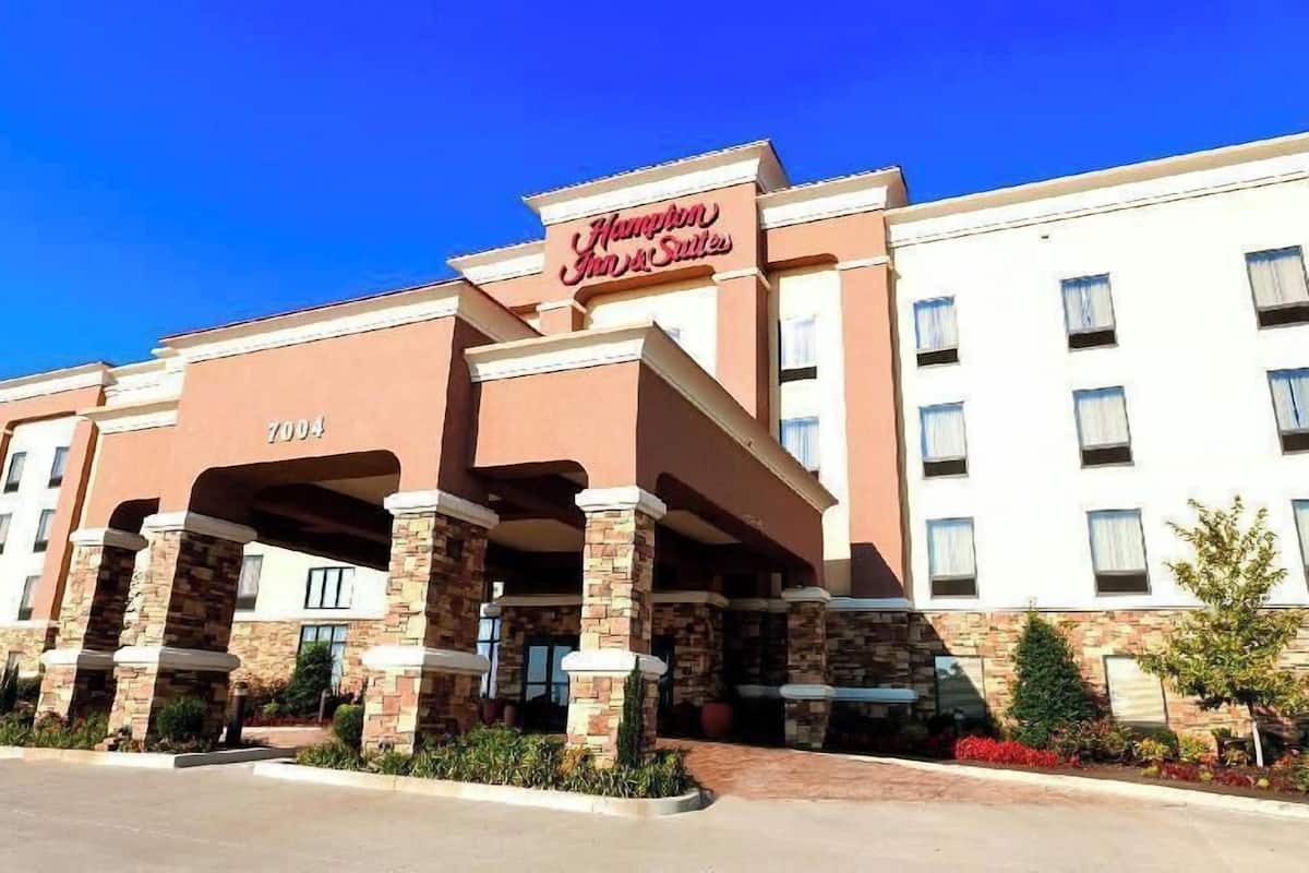Hampton Inn & Suites -hotellin rakennus, jossa on kiviverhous, useita ikkunoita ja kirkkaan sininen taivas.