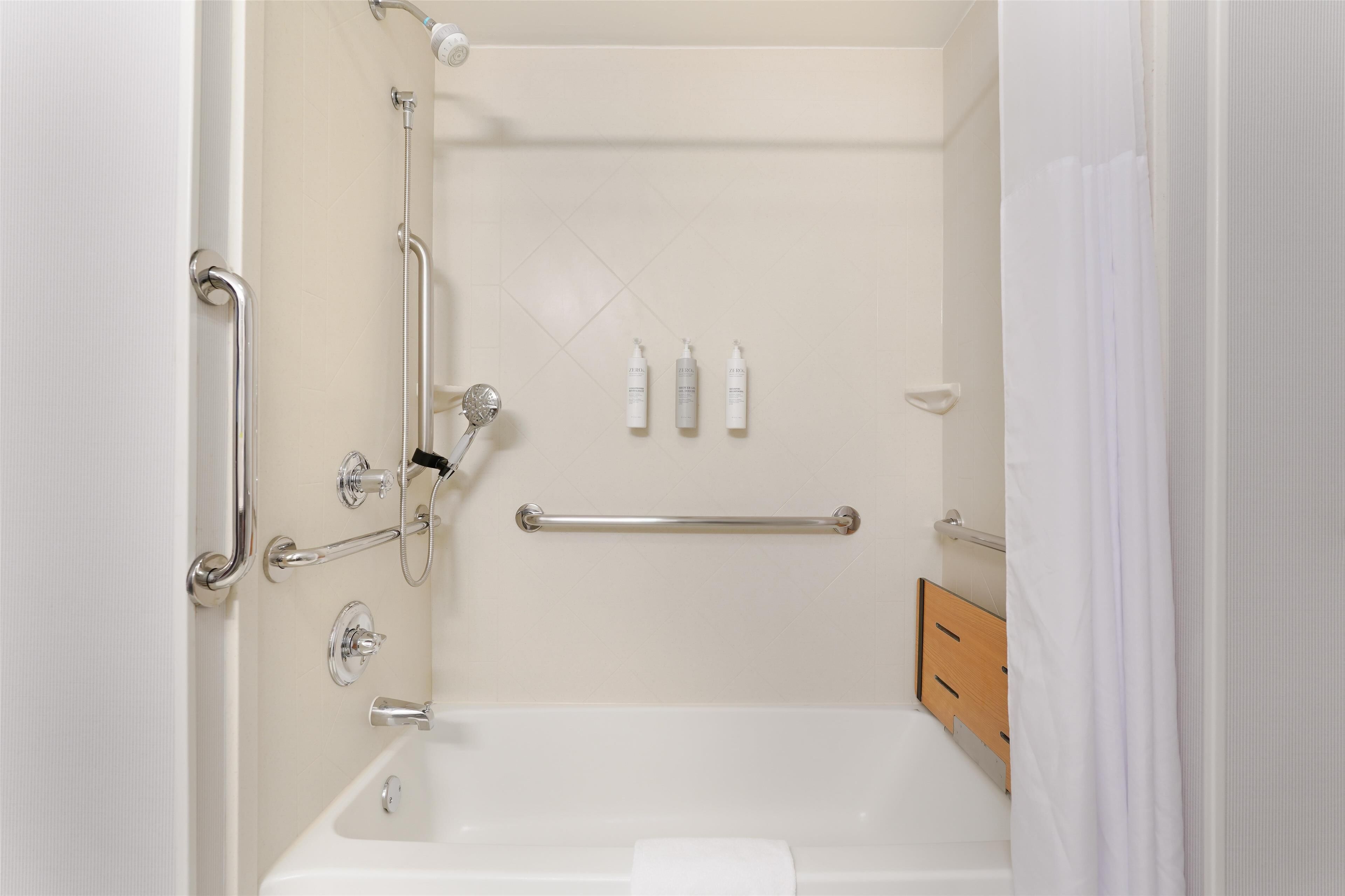 A bathroom with a bathtub, grab bars, a shower head, and a towel rack.