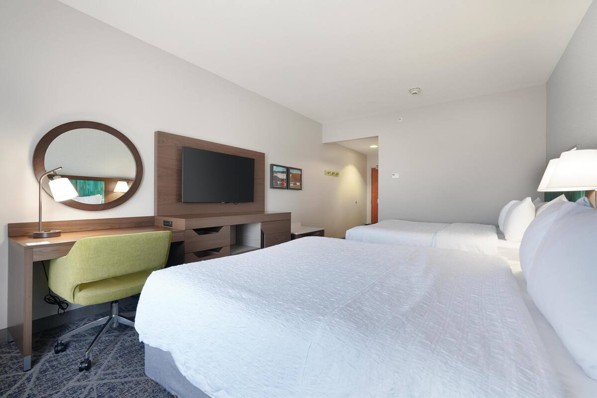 Hotellihuone, jossa on sänky, työpöytä tuolilla, televisio ja peili.