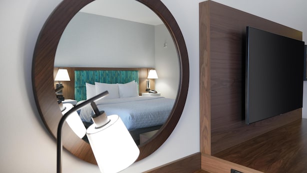 A hotel room with a large mirror, a bed with blue bedding, two bedside lamps, and a flat-screen TV mounted on the wall. - Hampton Inn & Suites Tulsa/Tulsa Hills (Tulsa)