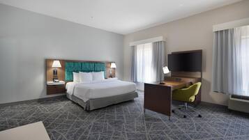 Habitación de hotel con una cama grande, un escritorio, dos lámparas, un televisor y una ventana con cortinas.