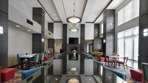 A modern hotel lobby with a long dining table, comfortable seating, a fireplace, and large windows. - Hampton Inn & Suites Tulsa/Tulsa Hills (Tulsa)