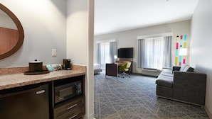 A hotel room with a kitchenette, a sofa, a TV, and a patterned carpet. - Hampton Inn & Suites Tulsa/Tulsa Hills (Tulsa)