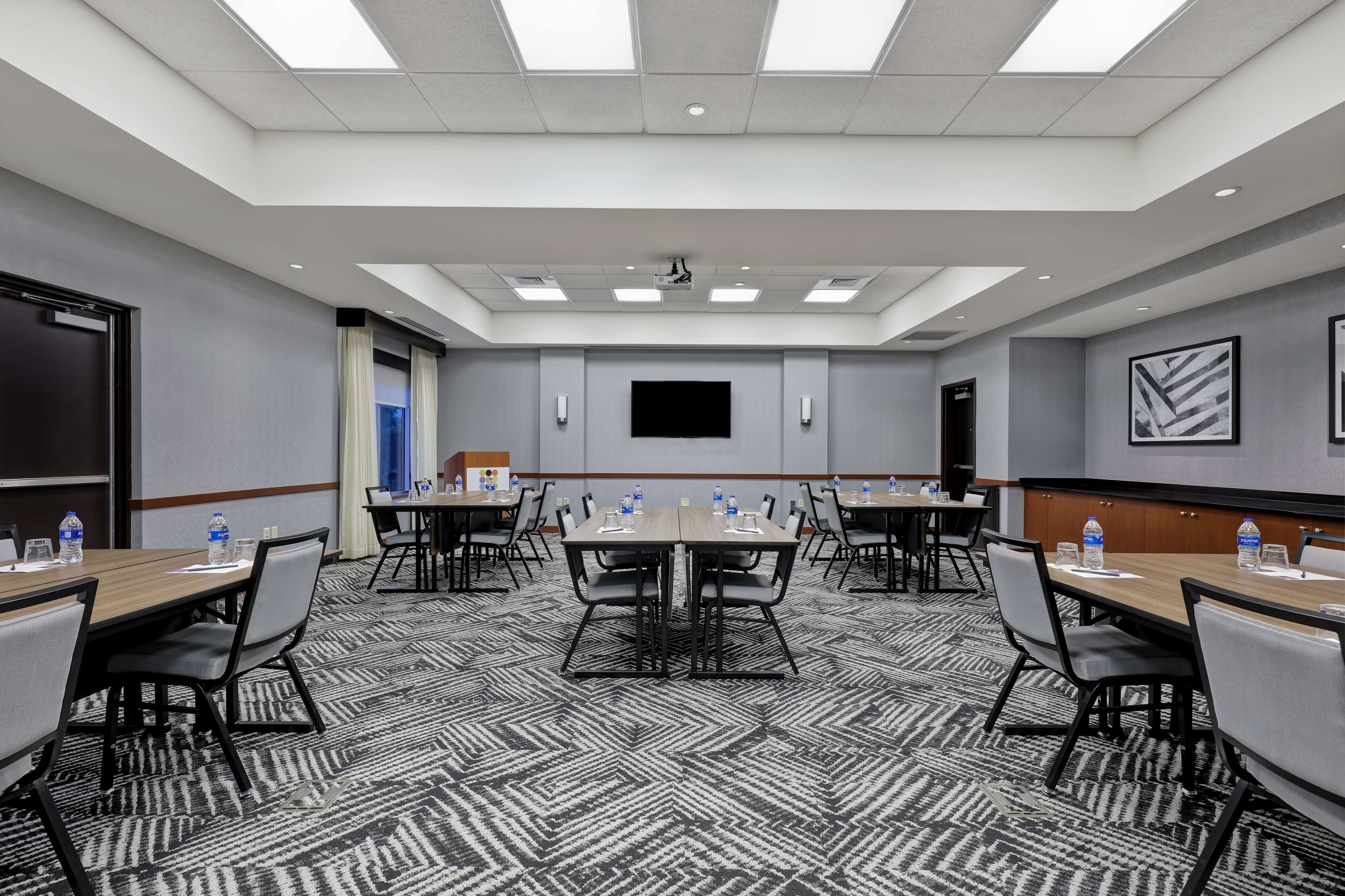 A conference room with multiple tables, chairs, a flat-screen TV, and a projector.