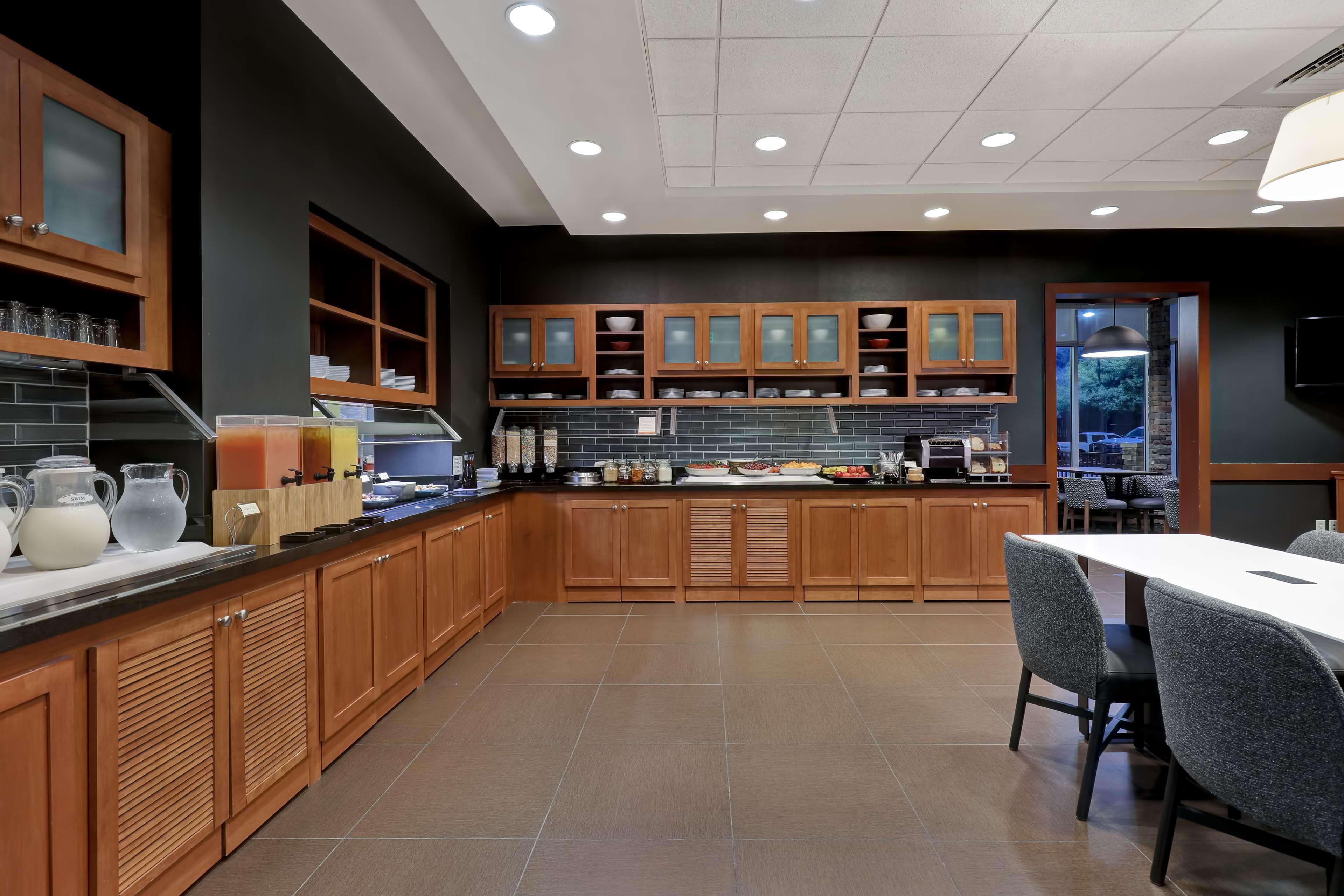 A modern kitchen with wooden cabinets, a dining area with a table and chairs, and a view of the outside through a glass door.