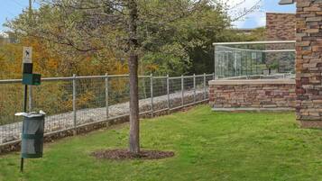 A fenced outdoor area with a pet waste station, a tree, and a stone building with a glass balcony.