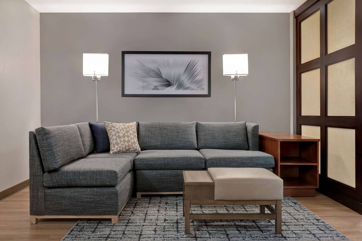 Ein modernes Wohnzimmer mit einem grauen Ecksofa, einem kleinen Holztisch und einem gerahmten abstrakten Kunstwerk darüber.