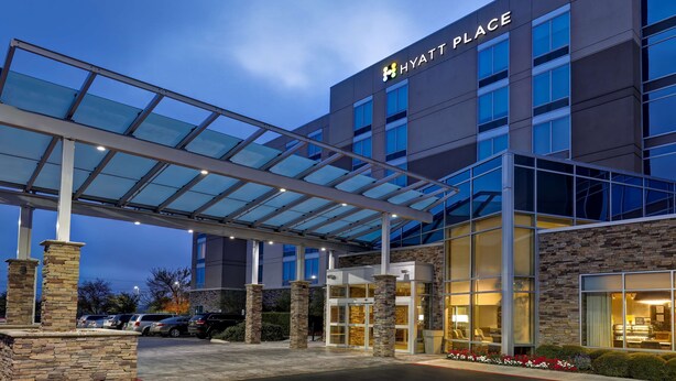 A modern Hyatt Place hotel with a glass entrance, stone pillars, and a covered walkway.