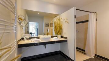 Un baño moderno con un espejo grande, dos lavamanos, una ducha y un florero con plantas altas.