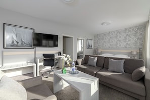 A modern hotel room with a sofa, a coffee table, a TV, and a bed with a headboard. - Hotel des Nordens by Sunday Hotels (Harrislee)