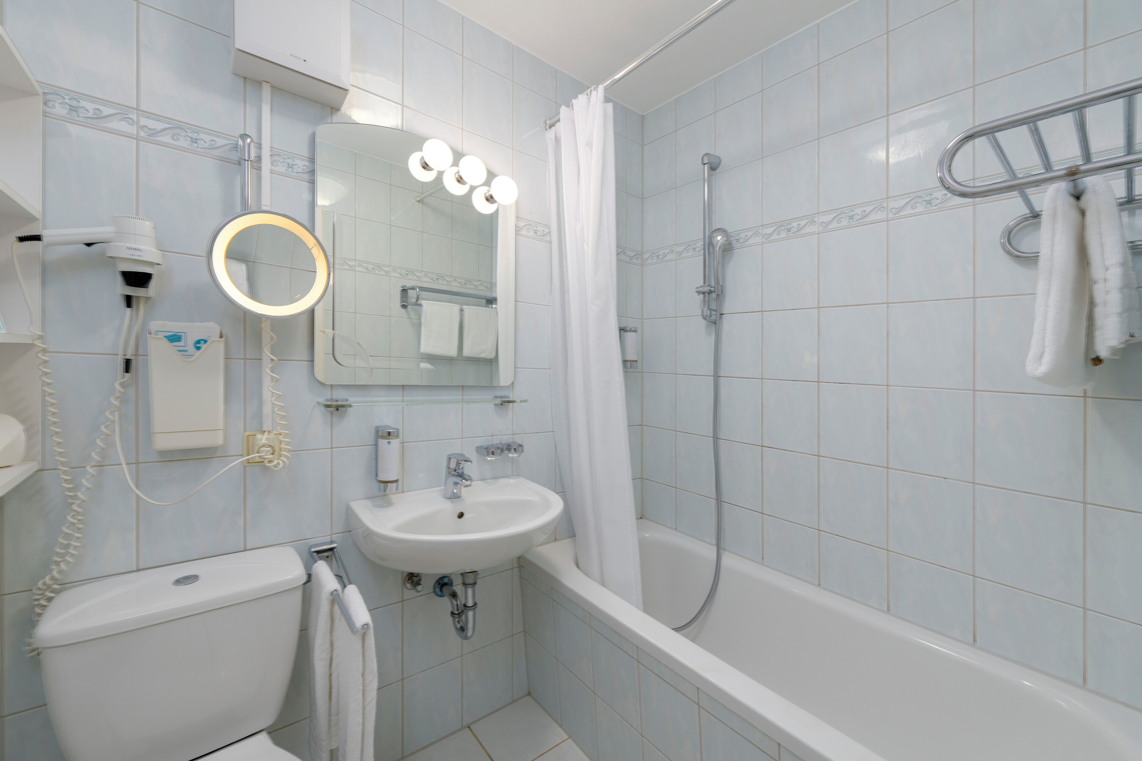 A bathroom with a toilet, sink, mirror, and shower.