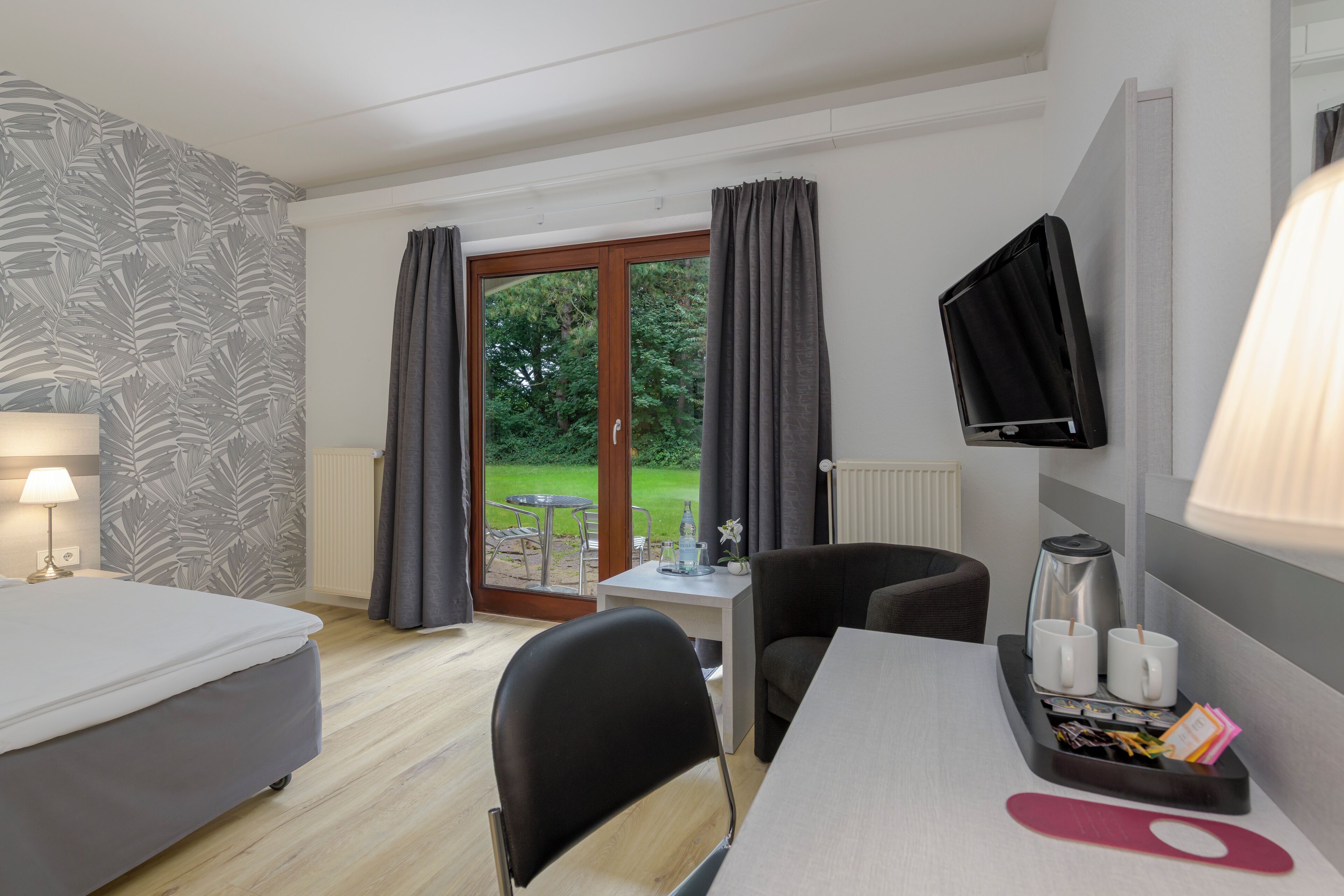 A hotel room with a bed, a desk, a chair, a TV, and a view of the outdoors.