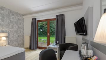 A hotel room with a bed, a desk, a chair, a TV, and a view of the outdoors.