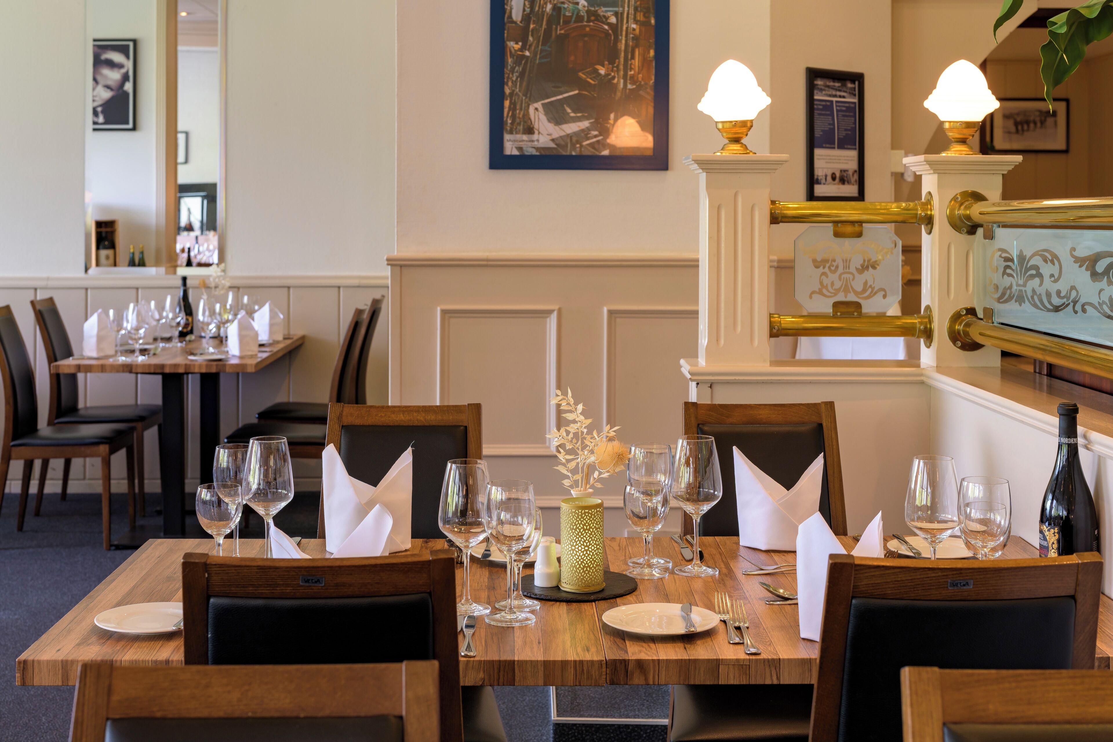 A dining area with wooden tables set for a meal, complete with wine glasses, plates, and cutlery.