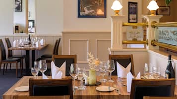 A dining area with wooden tables set for a meal, complete with wine glasses, plates, and cutlery.