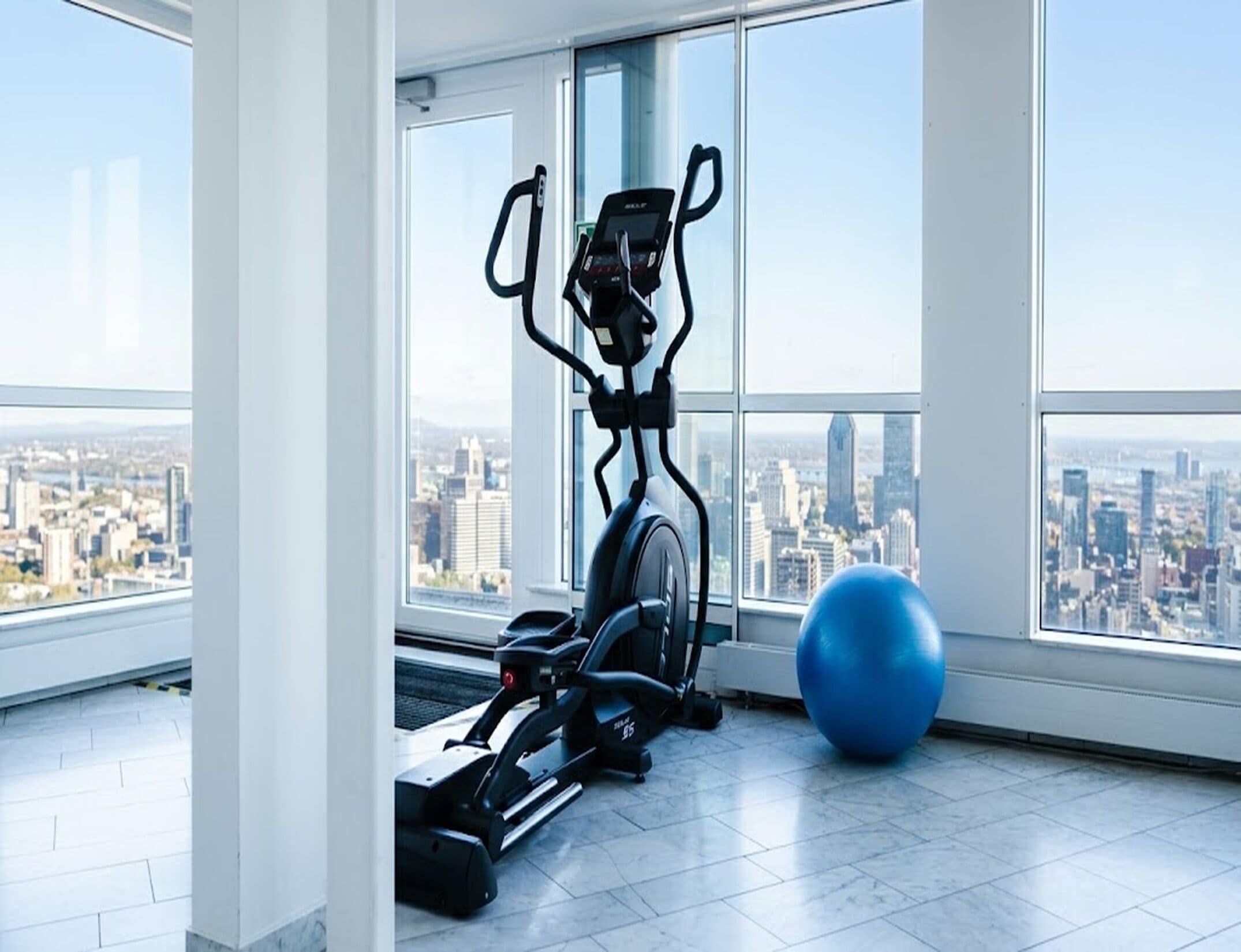 A gym with exercise equipment and a large window with a city view.