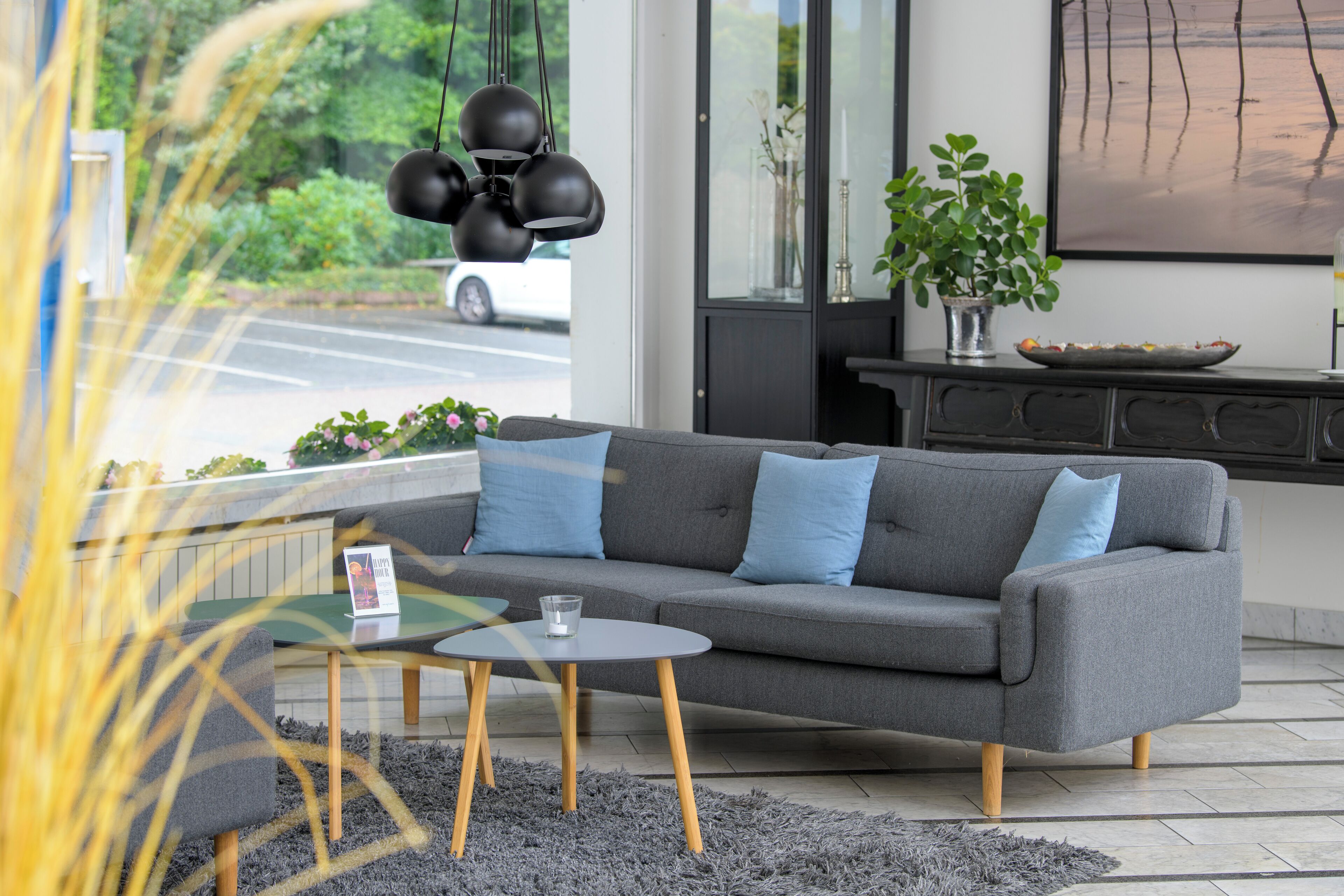 A modern living room with a grey sofa, blue cushions, a small round table, and a glass of water.