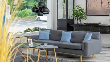 A modern living room with a grey sofa, blue cushions, a small round table, and a glass of water.