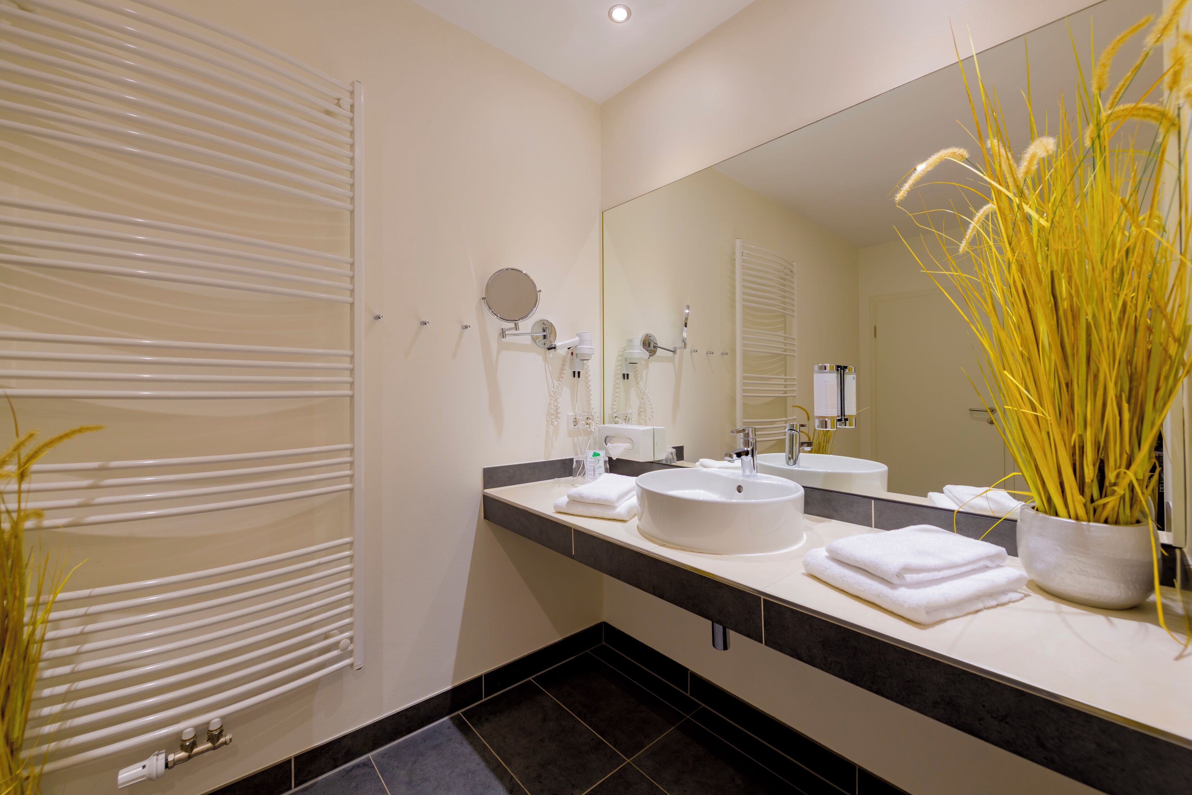 Un baño moderno con un espejo grande, dos lavamanos, un tendedero para toallas y un radiador.