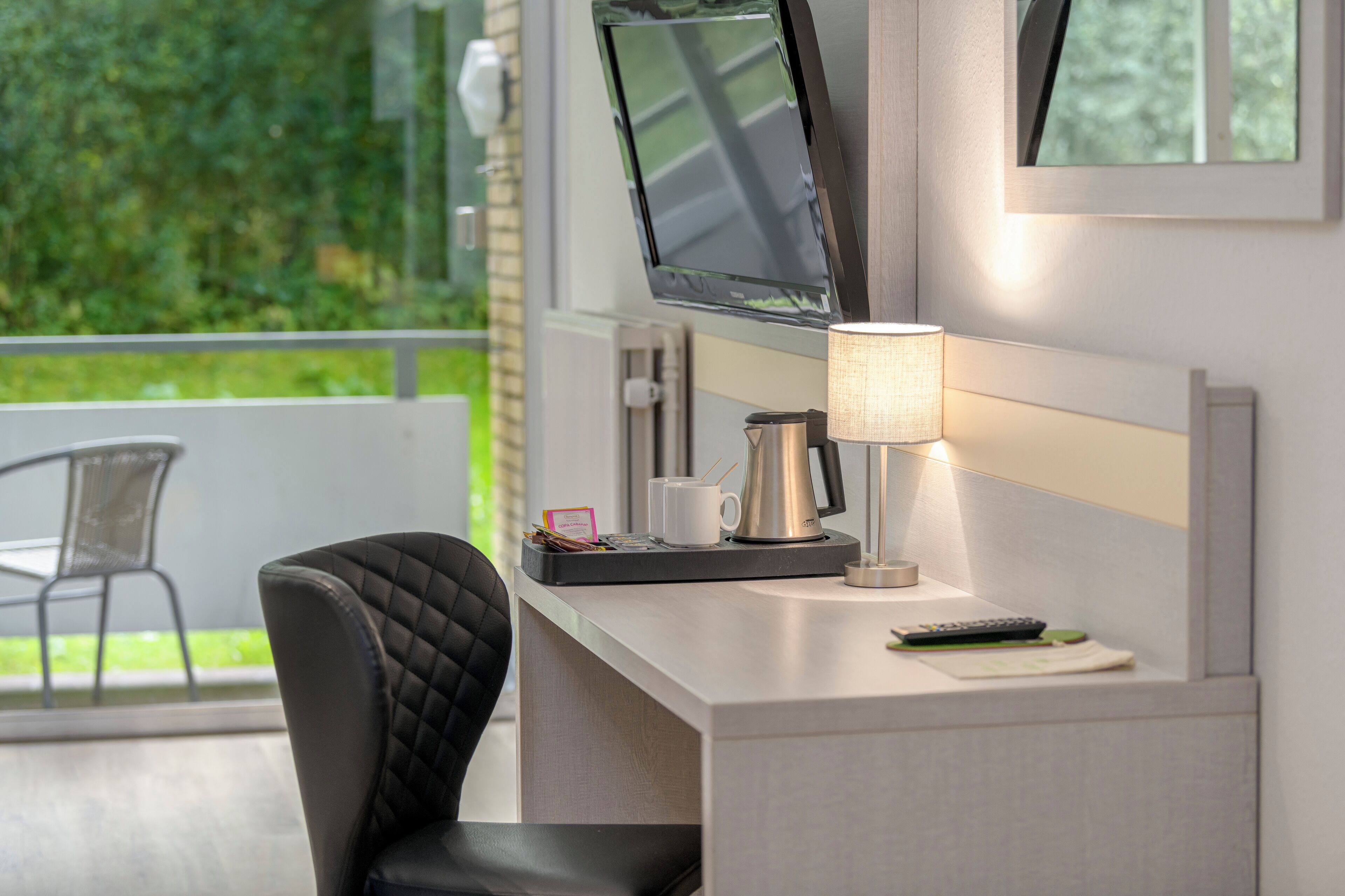 Una habitación de hotel con escritorio, una silla, televisor, lámpara y cafetera.