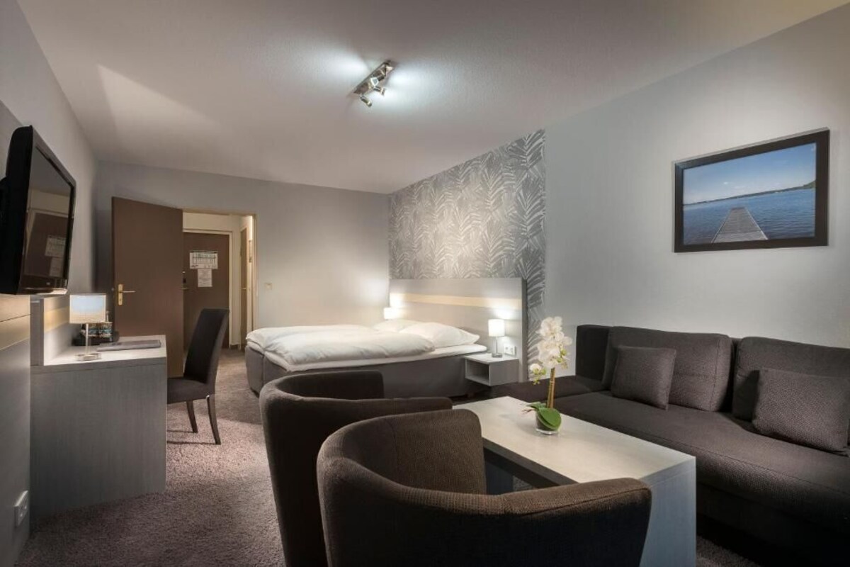A hotel room with a bed, a desk, a sofa, a TV, and a wall-mounted picture.