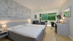 A modern hotel room with a large bed, a desk with a computer, a sofa, and a view of greenery outside. - Sunday Hotel des Nordens (Harrislee)