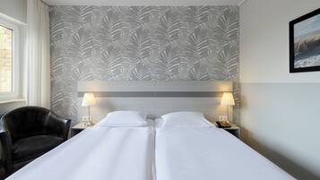 Ein Hotelzimmer mit einem Doppelbett, zwei Nachttischlampen, einem schwarzen Ledersessel und einer Wand mit Muster.