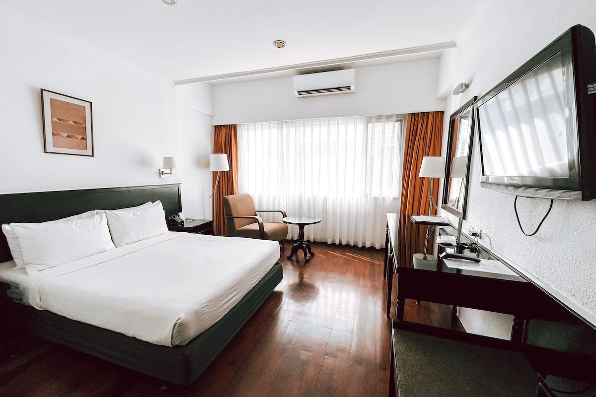 Een hotelkamer met een bed, een bureau, een stoel, een televisie en een airconditioning.