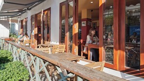 Un café al aire libre con mesas y sillas de madera, ventanas amplias y una valla de madera.