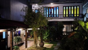 Un edificio moderno con un área exterior techada, plantas en macetas y un camino de ladrillo.
