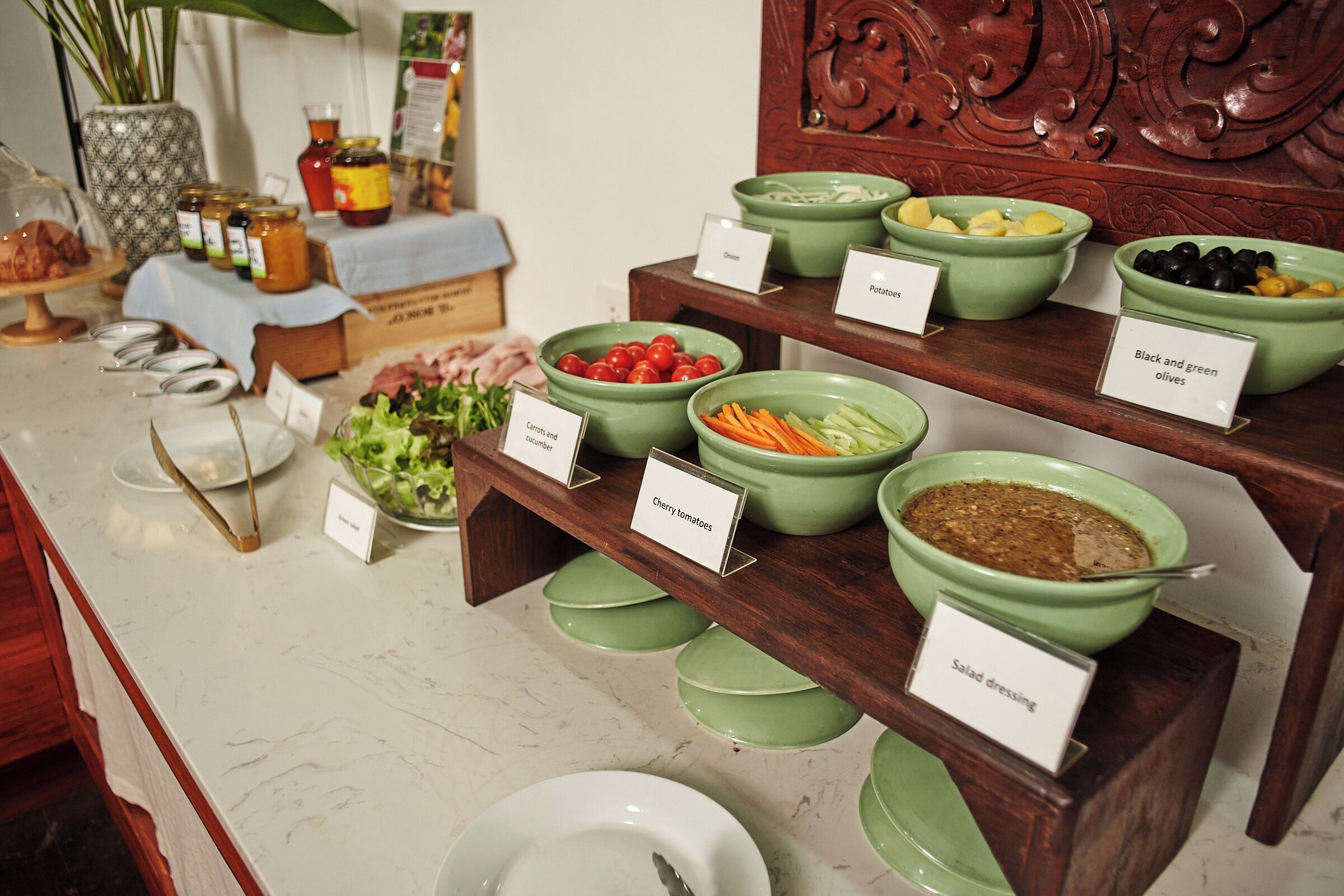 A buffet with labeled bowls of various foods such as salad dressing, carrots, and tomatoes.